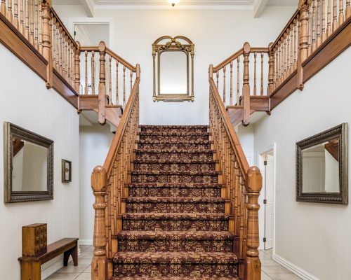 A big wooden staircase with a vintage carpet inside an apartment with white walls