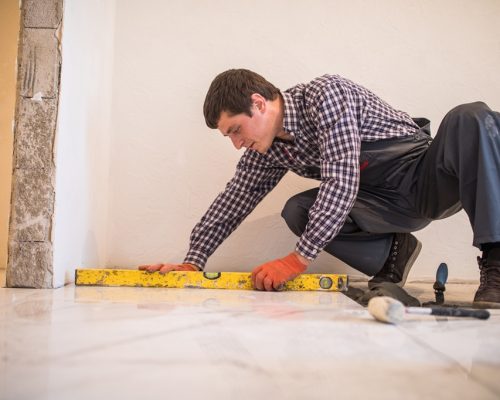 Home tile improvement - handyman with level laying down tile floor