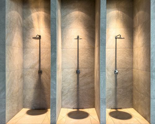 Architectural view of three shower niches with warm accent lighting and expressive stone texture. Refined premium minimalism.